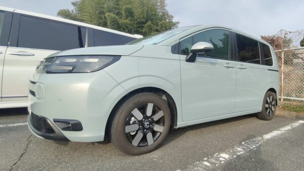 屋外駐車場に停めた淡いブルー系の新型フリードのサイド外観